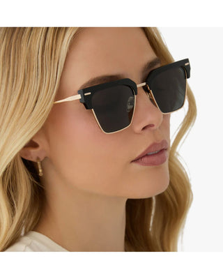 Woman wearing black sunglasses with gold frames on a white background