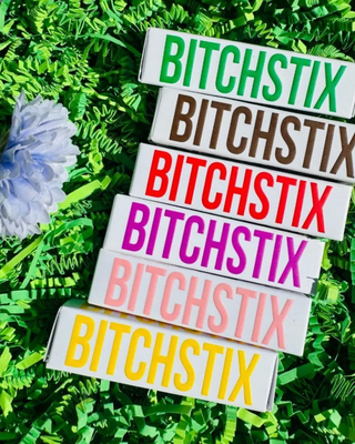6 bitchstix lip balm boxes with flower on green crumpled paper background 