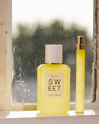 Two yellow perfume bottles labeled 'Sweet' by Ellis Brooklyn on a windowsill.