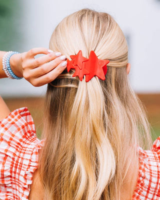 Person with blonde hair wearing a red hair clip, wearing a red and white checkered shirt.