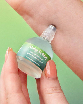 Hand holding a small bottle of Aloha Friday perfume oil against a green background