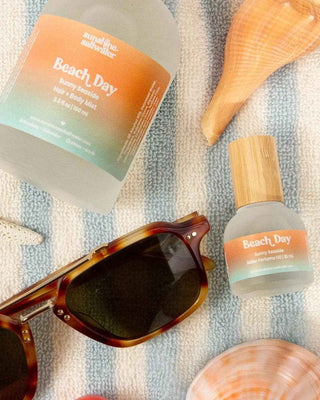 Two bottles labeled 'Beach Day' with sunglasses and shells on a striped fabric background