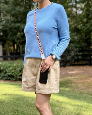 Person wearing a blue sweater and beige shorts standing outdoors with greenery in the background