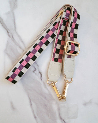 Checkered phone strap with gold hardware on a marble surface