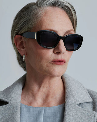 Woman wearing sunglasses and a gray coat against a plain background