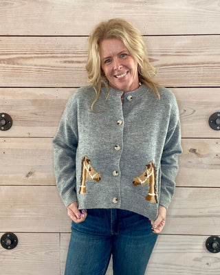 Woman wearing a gray cardigan with horse designs against a wooden background
