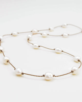 Tula Traveler white pearls spaced along knotted brown rope, laid on a white background.