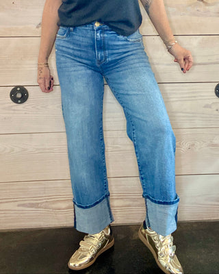 Woman wearing a blue t-shirt with a graphic design and jeans, standing against a wooden wall.