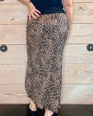 Woman wearing a black top and leopard print skirt against a wooden wall.