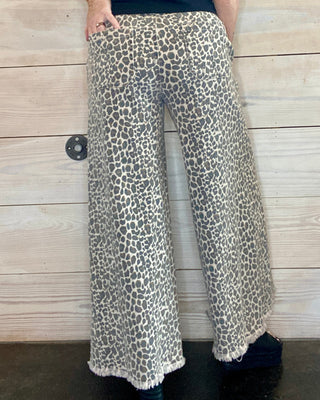 Person wearing a black t-shirt and leopard print pants against a wooden background