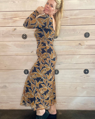 Woman wearing a patterned dress against a wooden wall.