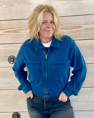 Person wearing a blue jacket and jeans standing against a wooden background