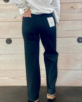 Person wearing a white long-sleeve shirt and dark pants against a wooden background