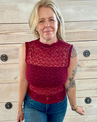 Woman wearing a red lace top and blue jeans against a wooden background