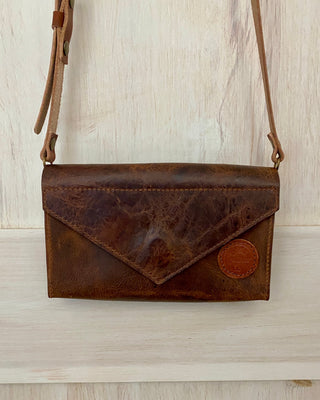 Brown leather crossbody bag on a light wooden surface