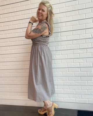 Brown gingham midi dress with smocked bodice, shoulder straps, and velvet trim accents styled for a feminine vintage-inspired outfit.