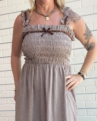 Brown gingham midi dress with smocked bodice, shoulder straps, and velvet trim accents styled for a feminine vintage-inspired outfit.