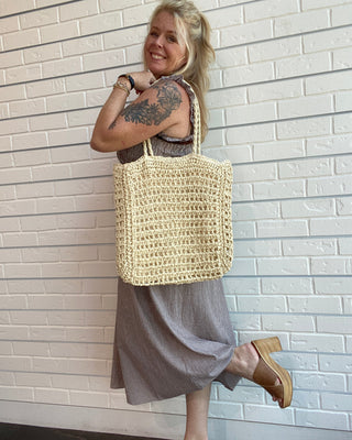 Woman holding a woven bag against a white tiled wall