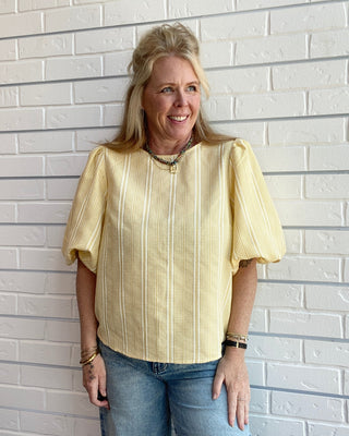 Yellow plaid women’s top with puff sleeves, round neckline, and statement bow back detail styled for a feminine spring outfit.