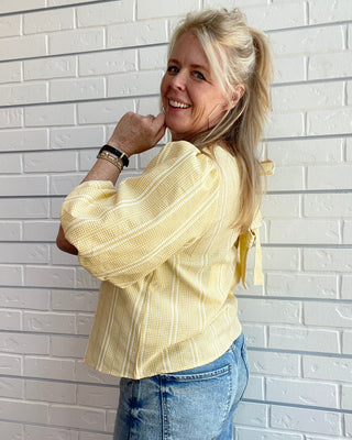 Yellow plaid women’s top with puff sleeves, round neckline, and statement bow back detail styled for a feminine spring outfit.
