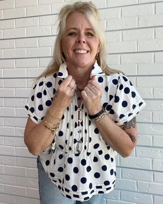 Woman wearing a polka dot blouse against a white brick wall