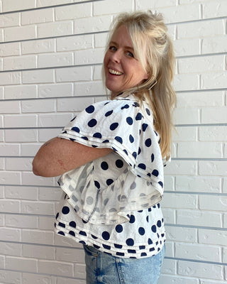 Woman wearing a polka dot shirt and jeans against a white brick wall