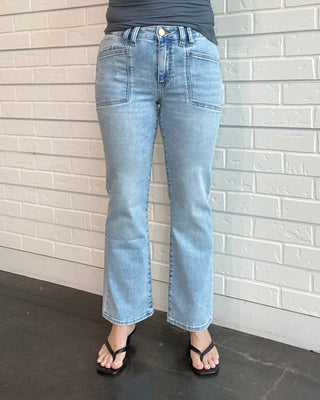 Person wearing a blue tank top and jeans standing against a light brick wall.