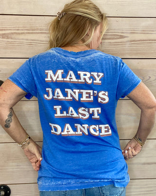 Person wearing a blue t-shirt with 'MARY JANE'S LAST DANCE' text on the back, standing against a wooden wall.