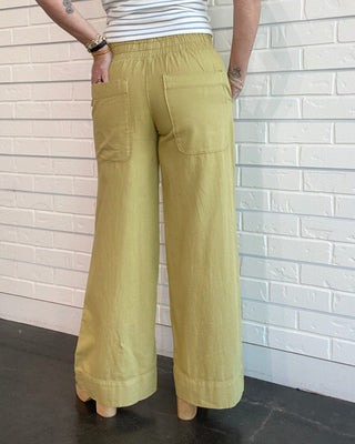 Person wearing a striped tank top and beige wide-leg pants against a white brick wall.