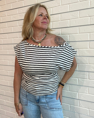 Woman wearing a black and white striped top and blue jeans against a beige brick wall.