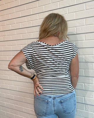 Person wearing a black and white striped shirt and blue jeans against a light brick wall.