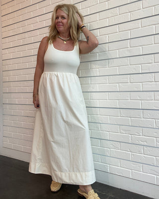 Woman wearing a white dress standing against a light-colored tiled wall.