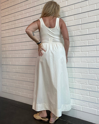 Woman wearing a white dress against a light-colored tiled wall.