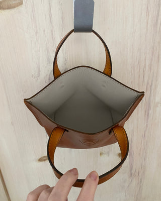 Brown leather handbag with a visible brand tag on a wooden surface