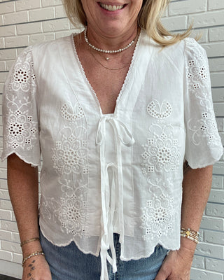 Woman wearing a white lace blouse against a light brick wall.