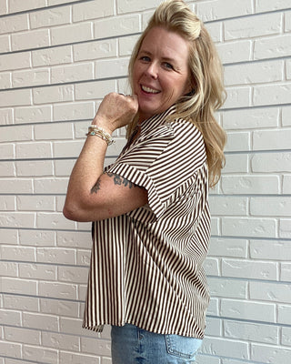 Woman wearing a striped shirt and jeans against a white brick wall
