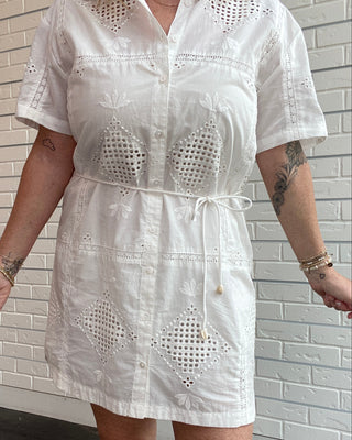 Person wearing a white embroidered dress against a brick wall.
