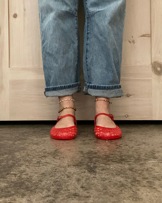 Person wearing blue jeans and red shoes standing on a concrete floor with wooden paneling in the background.