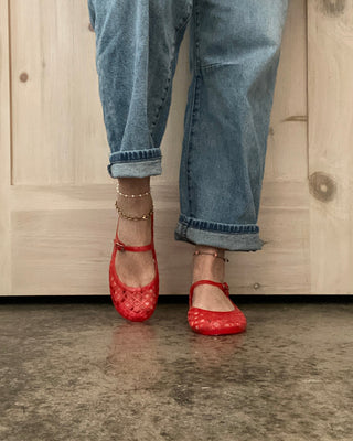 Person wearing red shoes and blue jeans standing on a concrete floor with a wooden door in the background.