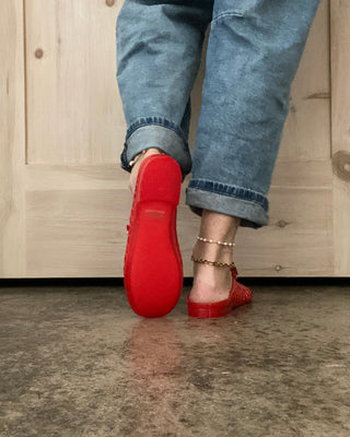 Red shoes worn with blue jeans on a concrete floor.