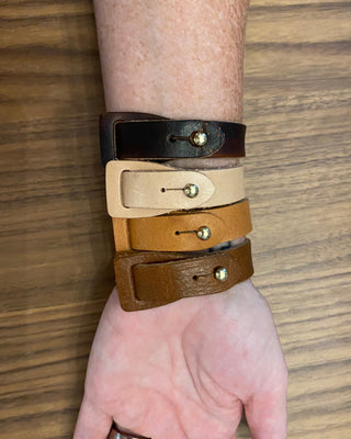 Four leather bracelets in black, beige, and brown on a wrist against a wooden background