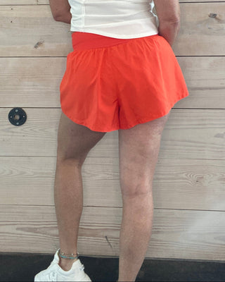 Person in a white top and orange skirt standing on a wooden floor.