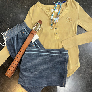 Yellow long-sleeve shirt with denim shorts and a brown belt on a dark surface