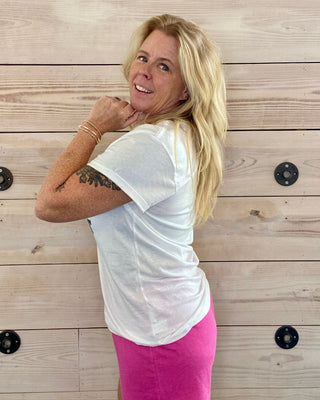 Woman in a white t-shirt and pink shorts standing against a wooden wall.