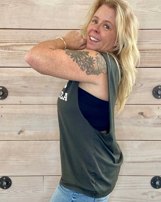 Woman wearing a charcoal tank top with text, standing against a wooden wall.