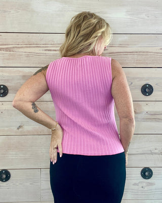 Person wearing a pink sleeveless top against a wooden wall.