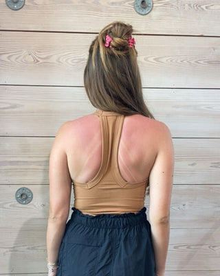 Person wearing a tan tank top and navy shorts against a wooden wall.