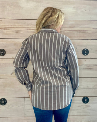 Person wearing a striped blazer and blue jeans against a wooden background