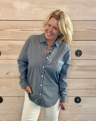 Woman wearing a striped shirt and white pants standing against a wooden wall.