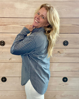 Woman wearing a blue striped shirt against a wooden wall.